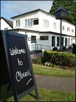 A photograph of the Olivers Restaurant sign with the restaurant in the background